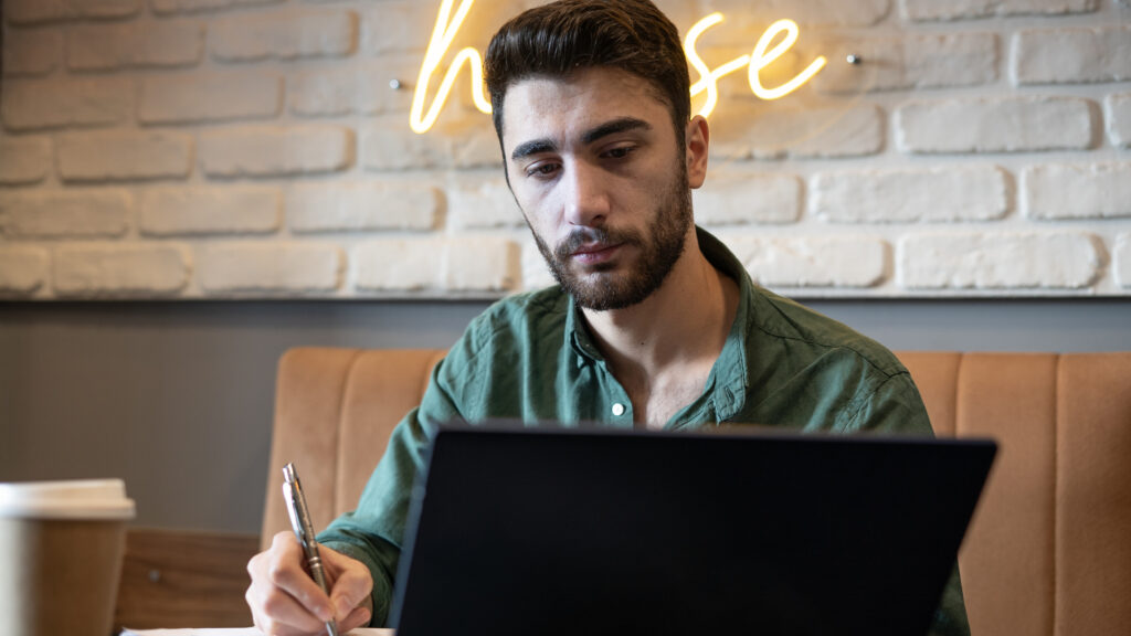 Handsome businessman taking notes while working with laptop in office