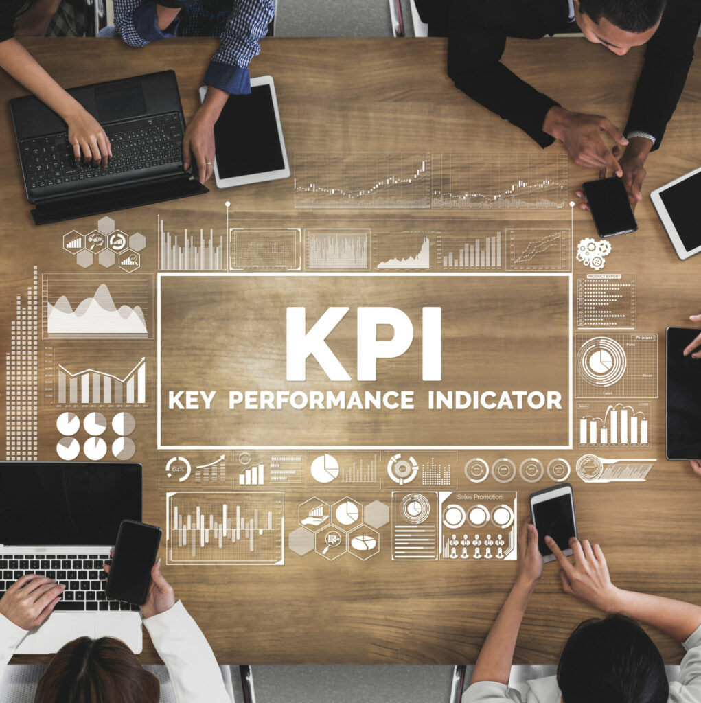Key Performance Indicators (KPI) is written on a table surrounded by graphs and people working
