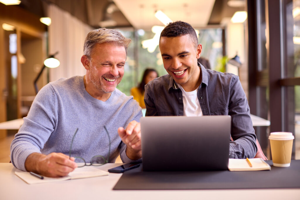 Man sitting and pointing to a laptop screen in front of another man