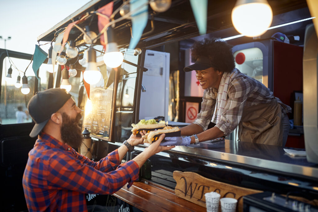 caucasian beardy hipster taking two sandwiches from polite female african-american employee in fast food service