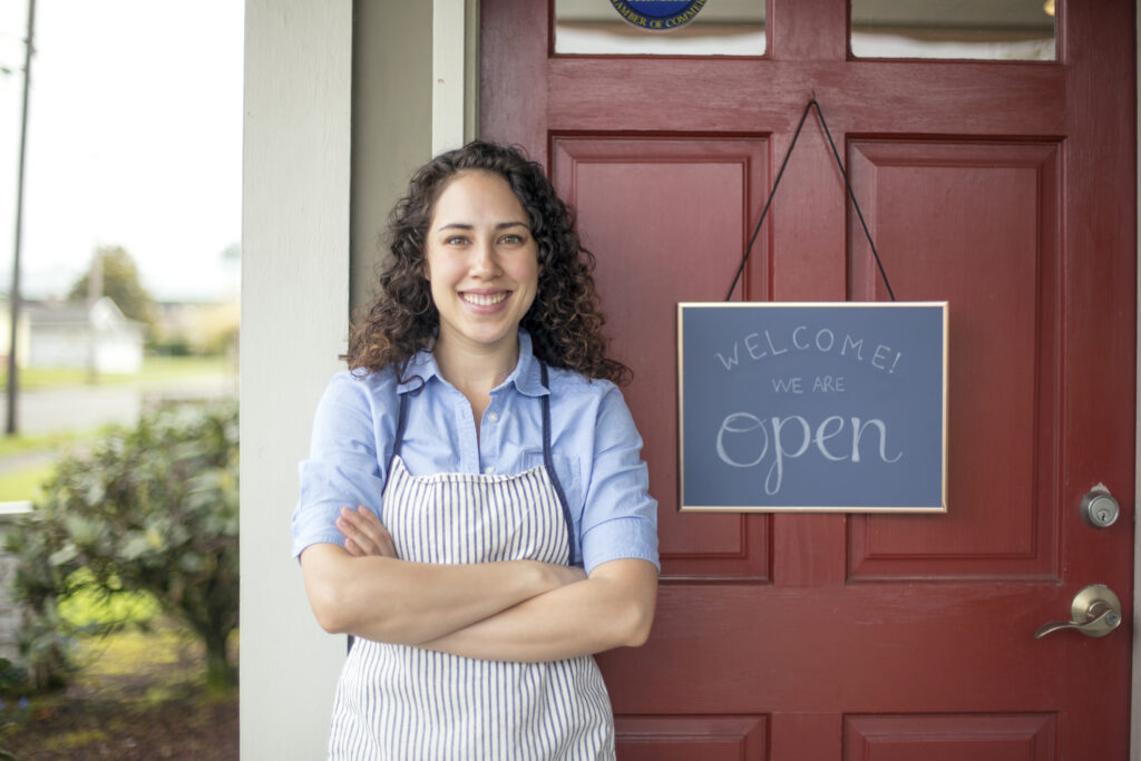 Female business woman smiling in front of her open business sign