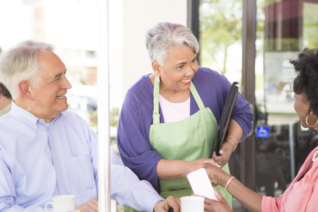 Senior adult female business owner working at her outdoor cafe/restaurant shaking hands with an angel investor