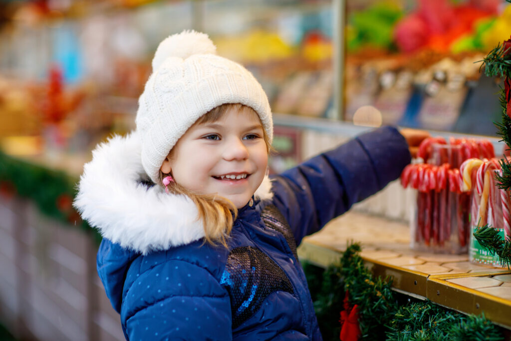 Little cute preschool girl buying candy cane from a sweets stand