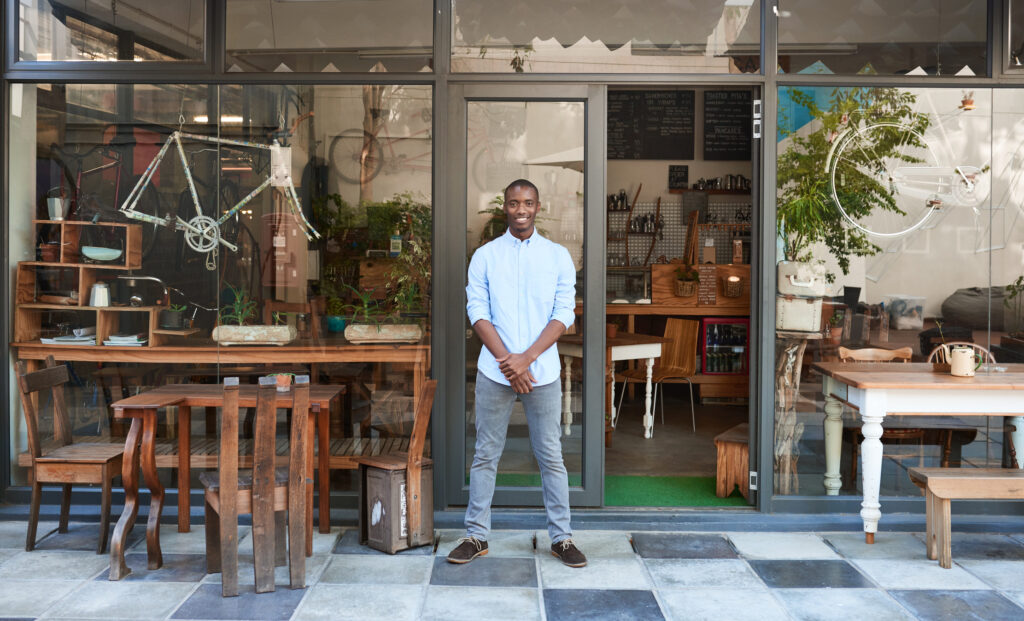 Smiling entrepreneur standing welcomingly in front of his cafe