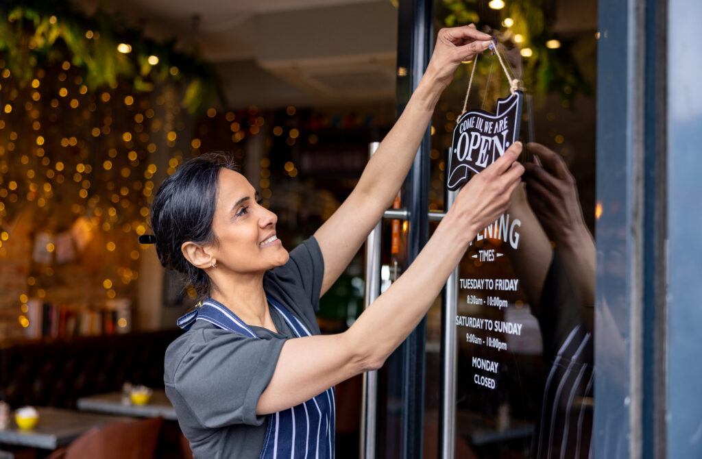 Business owner hanging an open sign on the door at a cafe