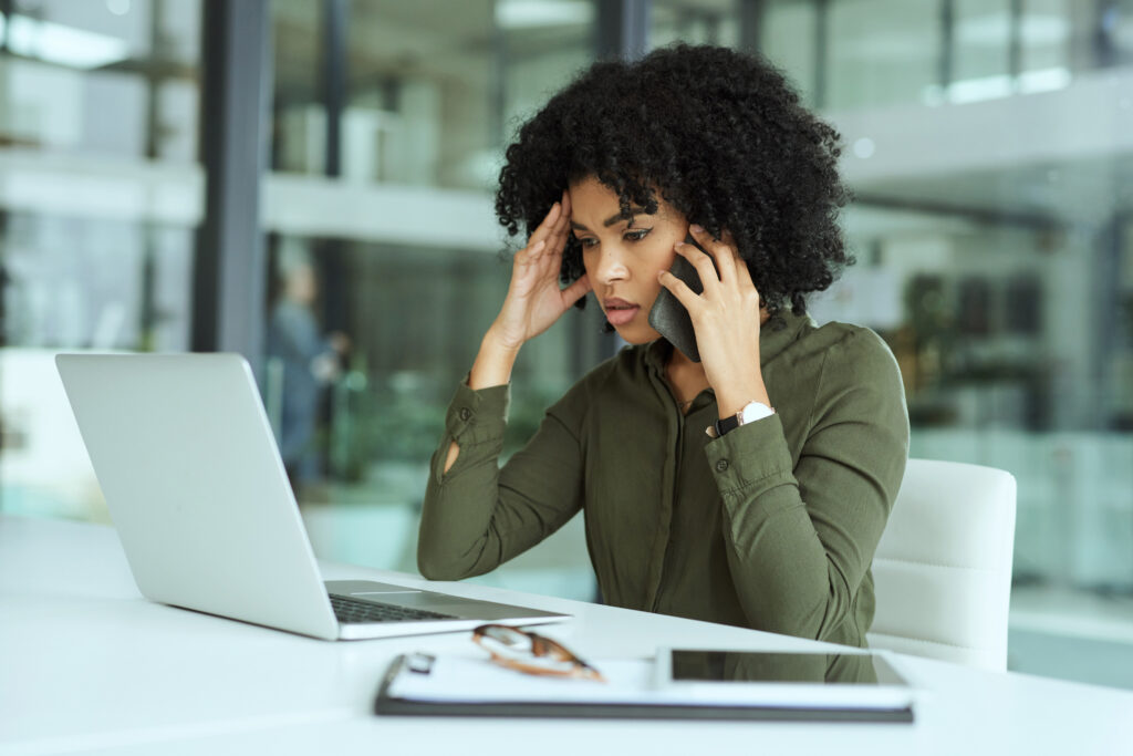 woman on her computer and on the phone looking frustrated