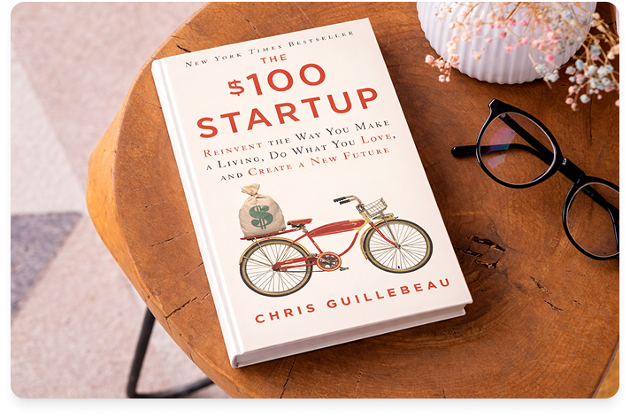 Image of $100 Startup book laying on a wood table.