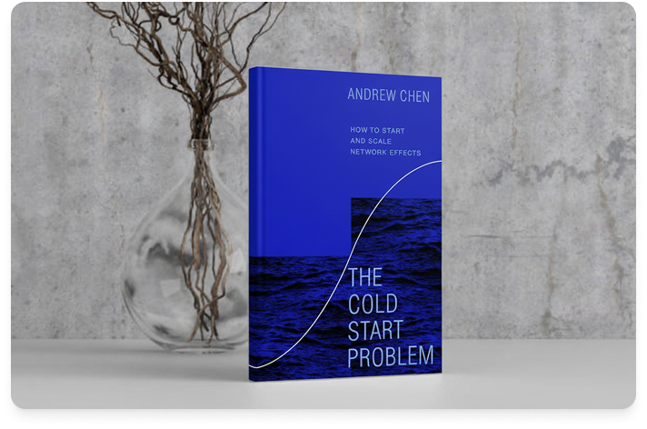 Image of the book The Cold Start Problem on a white desk with a gray marbled wall behind it, and branches displayed in a glass bulb vase.