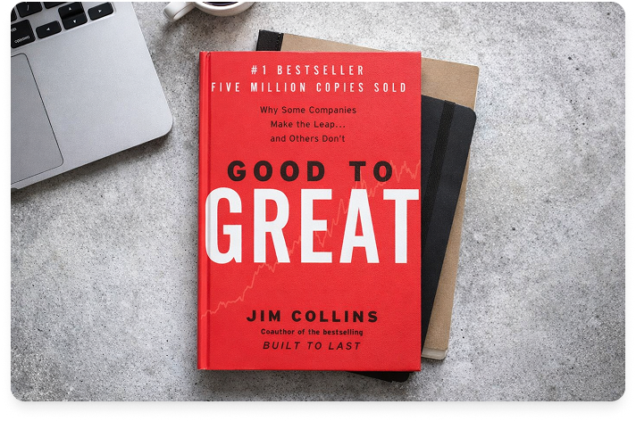 Image of the book Good to Great on a gray desk, sitting atop some other books and near a laptop.