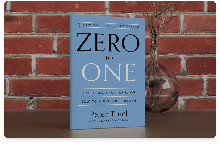 Image of the book Zero to One on a metal tabletop with a brick wall in the background and a plant in a glass bulb vase.