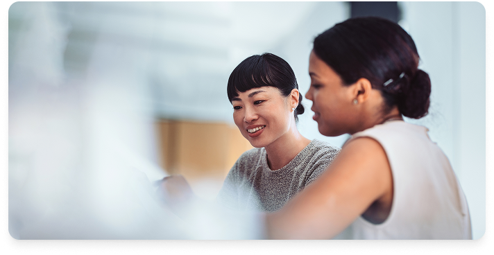 Two women collaborating in an office, both looking down at a desk with something on it.