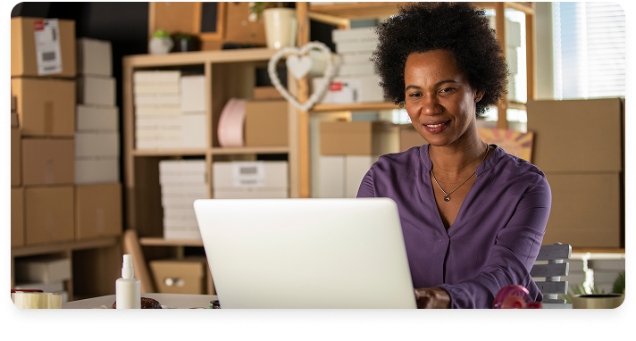 Business woman in purple blouse at a laptop in a small shipping room of a business.