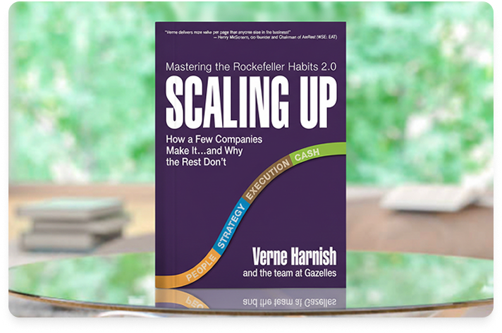 Image of the book Scaling Up on a reflective tray on a table in a nature setting with greenery behind it.