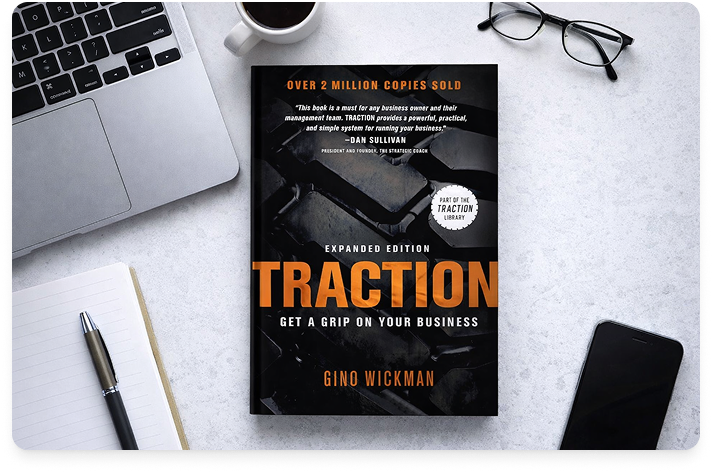 Image of the book Traction on a white desk with the corner of a laptop showing in the left corner and a pen below the computer.